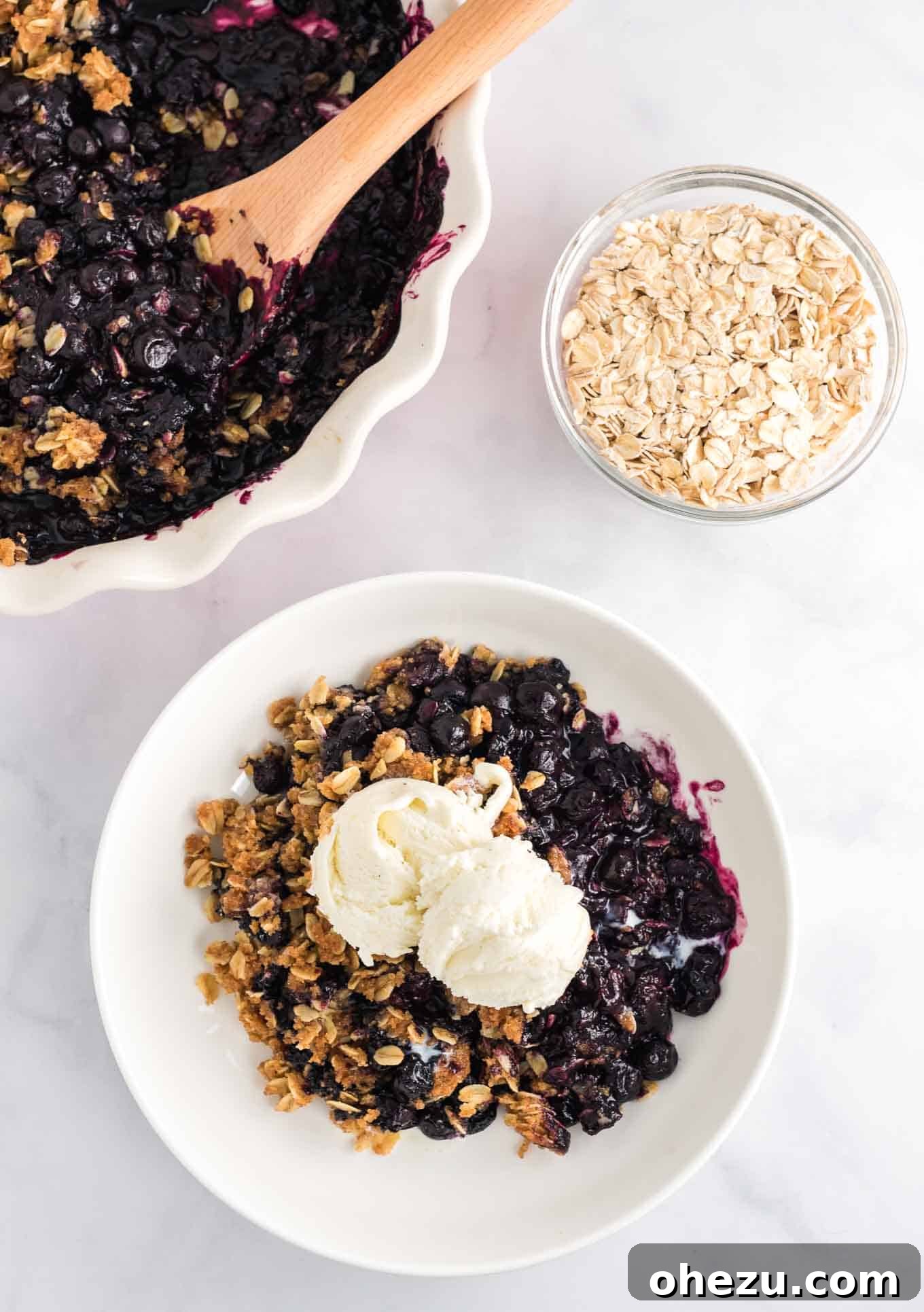 Blueberry crisp in a white bowl with two scoops of vanilla ice cream on top, ready for serving