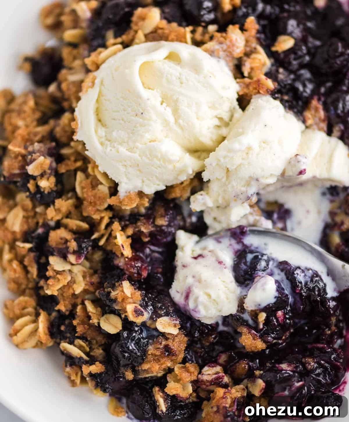 A silver spoon taking a bite of blueberry crisp and ice cream, showcasing the perfect combination