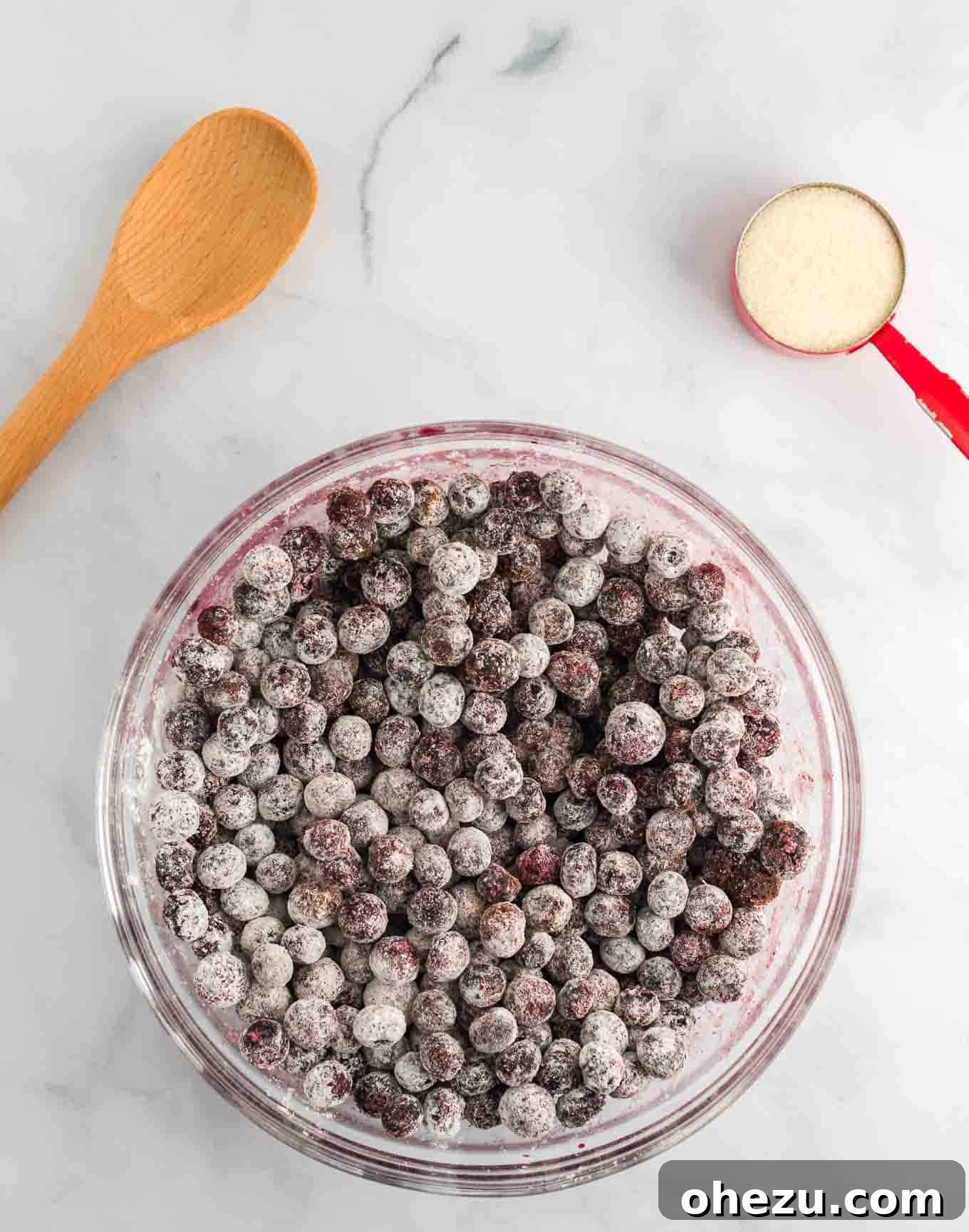 Frozen blueberries in a glass bowl mixed with sugar, cornstarch, and cinnamon, showing initial coating