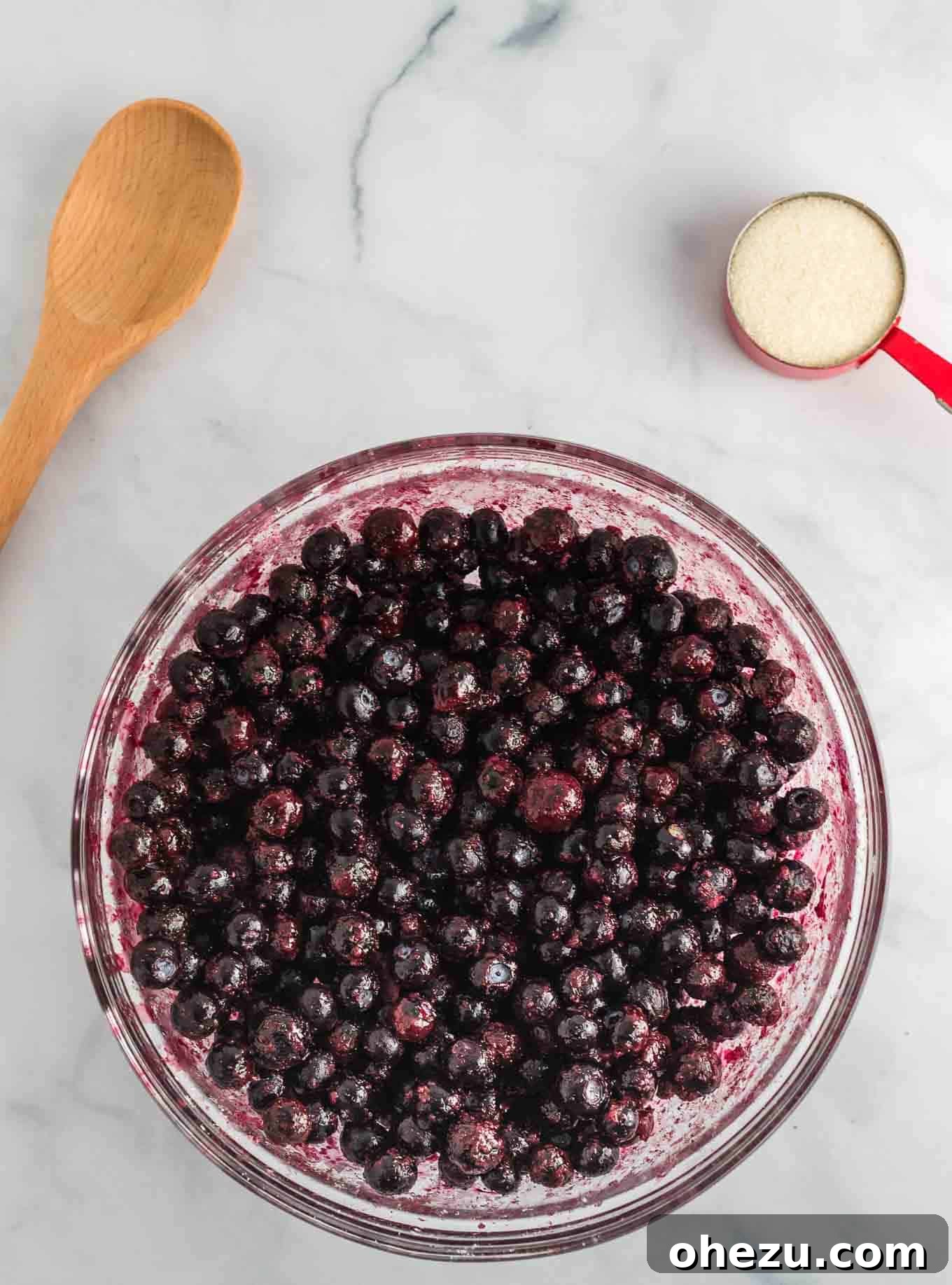 Partially defrosted frozen blueberries in a clear bowl after stirring, showing a more even coating