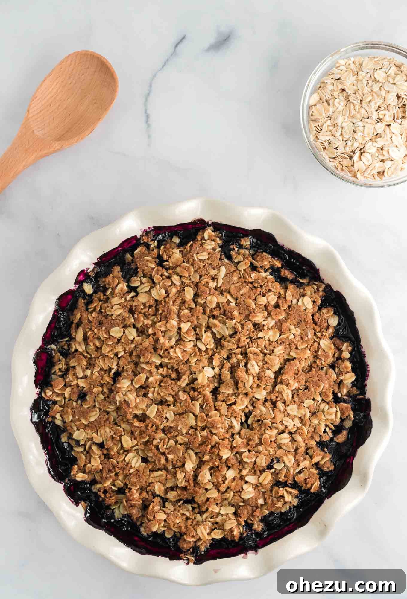 Finished blueberry crisp in a white rimmed pie dish, fresh from the oven, showing golden-brown topping