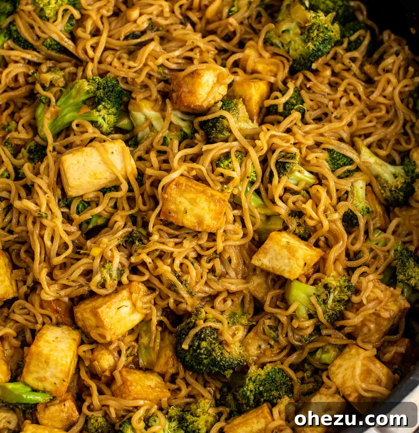 Close up of a spoonful of tofu, broccoli, and cooked ramen noodles, showing the texture and sauce coating