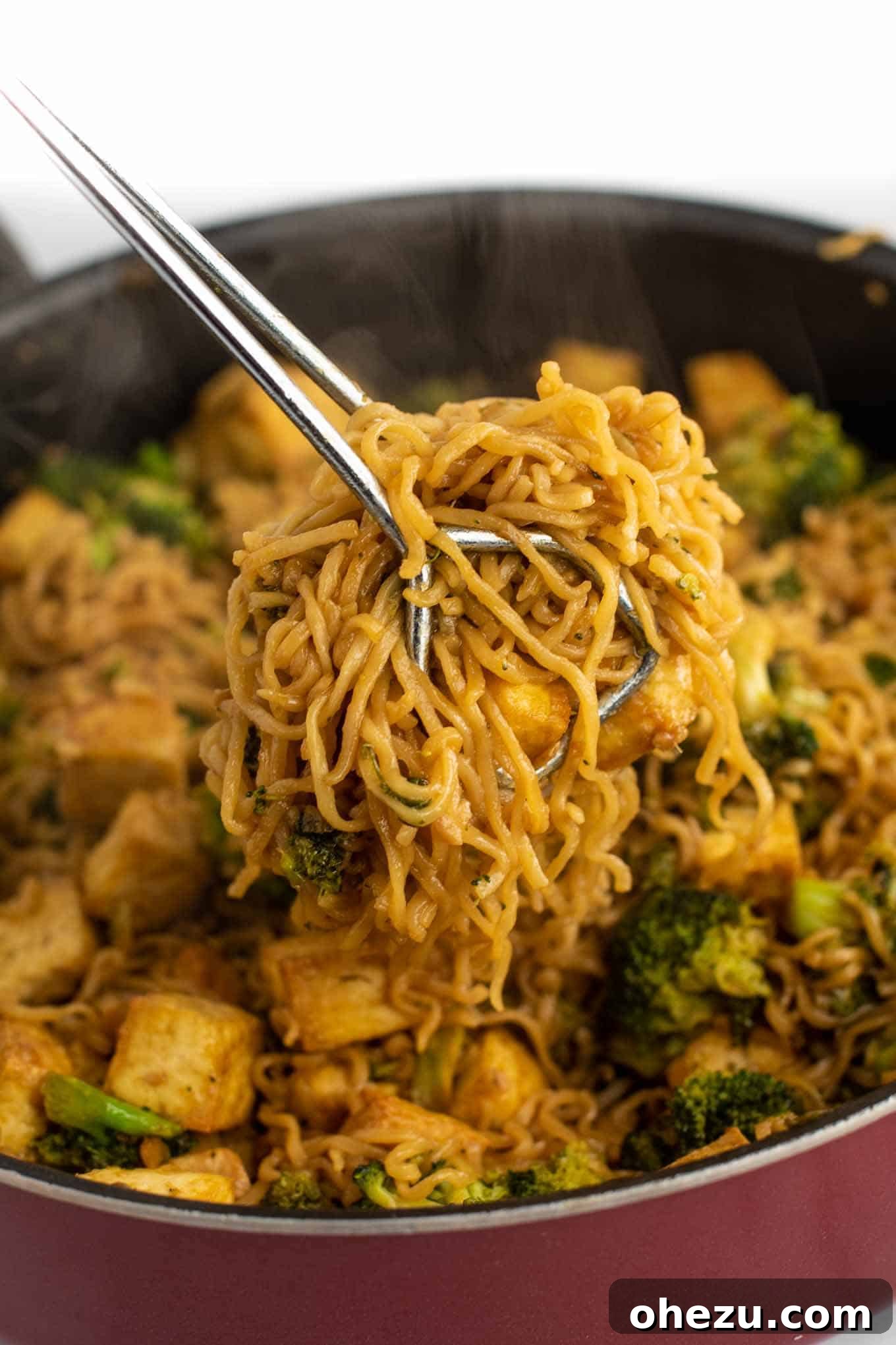 Tongs serving a portion of the delicious ramen noodle stir fry from a large pan