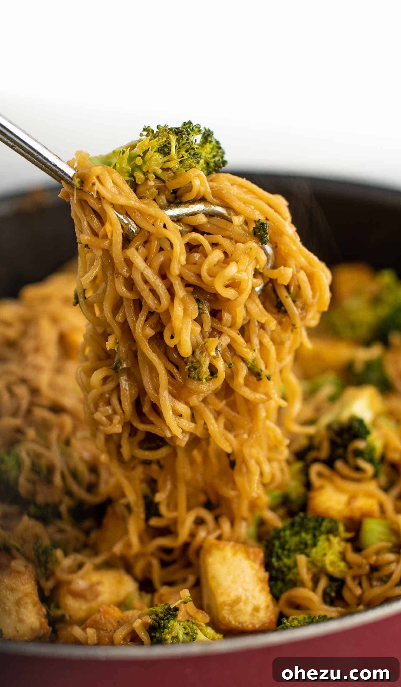 Tongs picking up a generous portion of broccoli tofu ramen noodles from a skillet