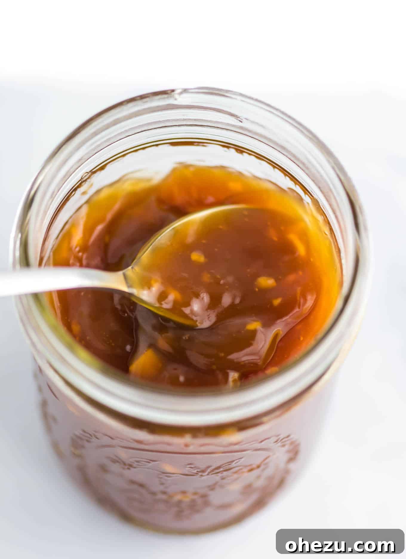 Zesty Orange Glaze 2 A spoon dipped into a mason jar filled with glossy, homemade orange sauce, highlighting its vibrant color and smooth texture.