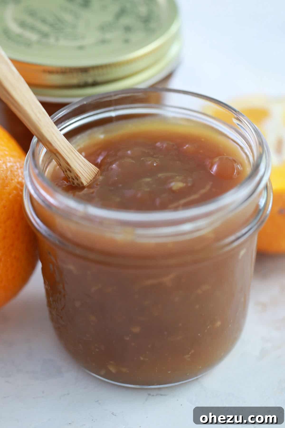 Zesty Orange Glaze 11 A glass jar filled with luscious orange sauce, with a wooden spoon resting inside, ready for serving.