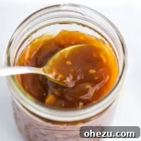 A spoon dipping into a bowl of orange sauce for chicken, highlighting the sauce's rich texture.