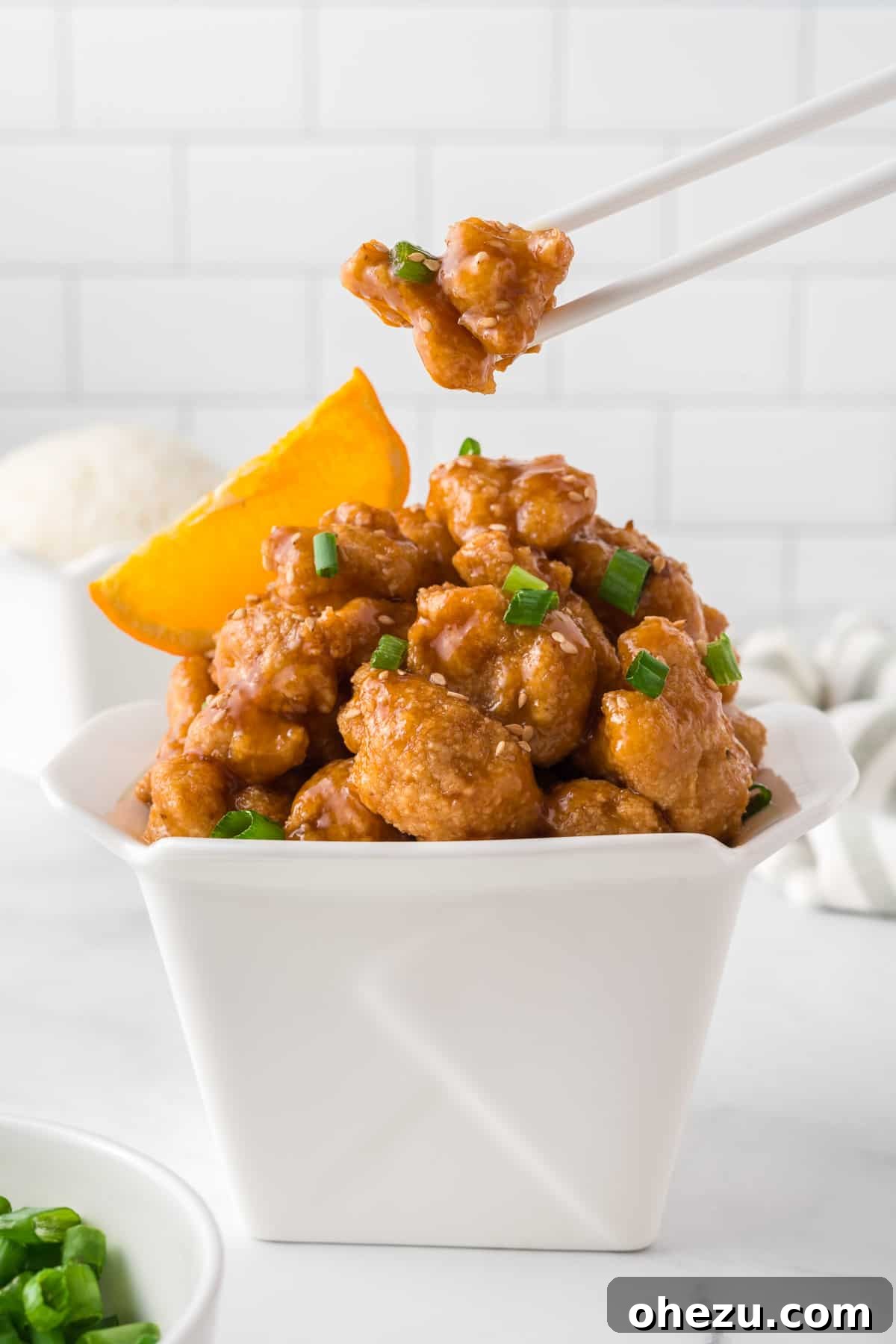 Zesty Orange Glaze 3 Crispy orange cauliflower served in a traditional white takeout container, garnished with green onions and sesame seeds, showcasing a delicious vegan alternative.