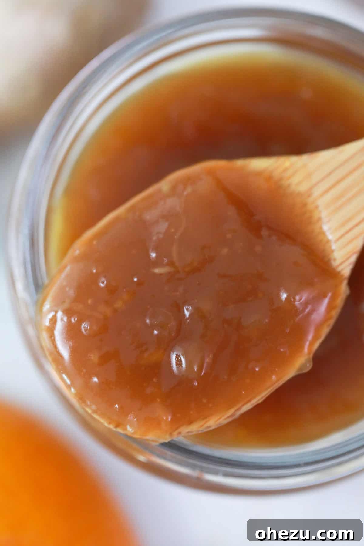 Zesty Orange Glaze 4 A wooden spoon holds a generous scoop of thick, glossy homemade Chinese orange sauce, illustrating its perfect consistency.