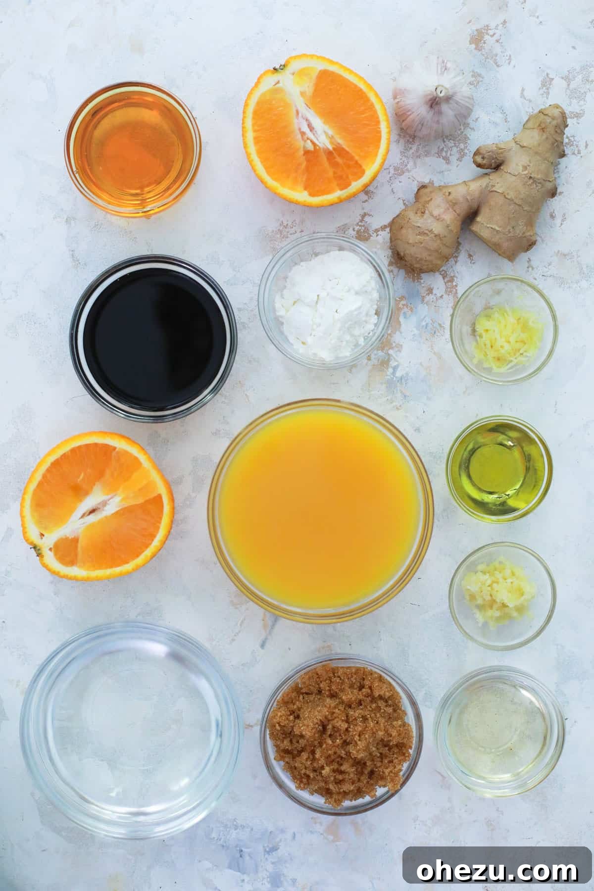 Zesty Orange Glaze 5 Various ingredients for orange sauce, including fresh orange juice, soy sauce, brown sugar, rice vinegar, minced garlic, and ginger, arranged in glass bowls on a white surface.