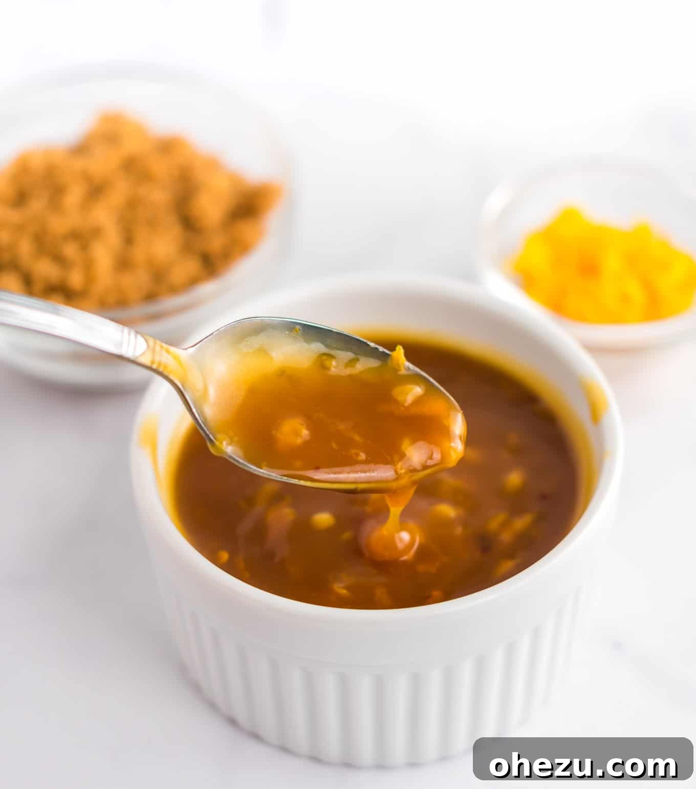 Zesty Orange Glaze 10 A spoon dipping into a bowl of rich, vibrant orange sauce, highlighting its thickness and inviting texture.
