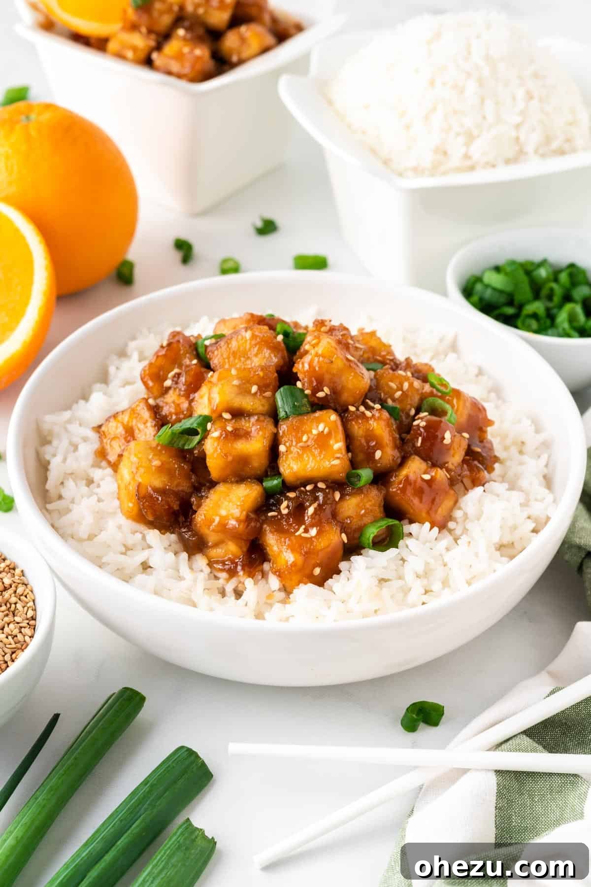 A beautifully presented bowl of crispy orange tofu served over fluffy white rice, garnished with fresh green onions and sesame seeds.