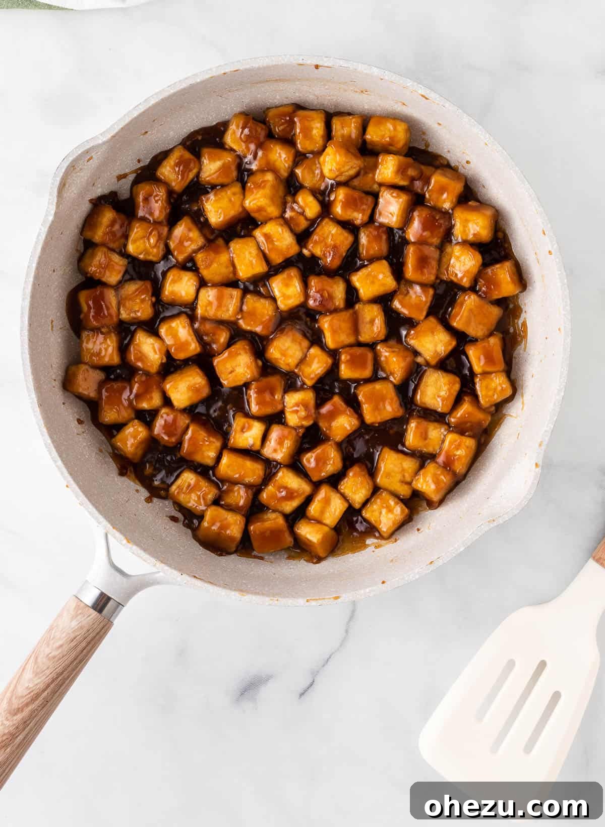 The vibrant orange sauce being poured into a skillet filled with crispy tofu cubes, ready to be tossed.