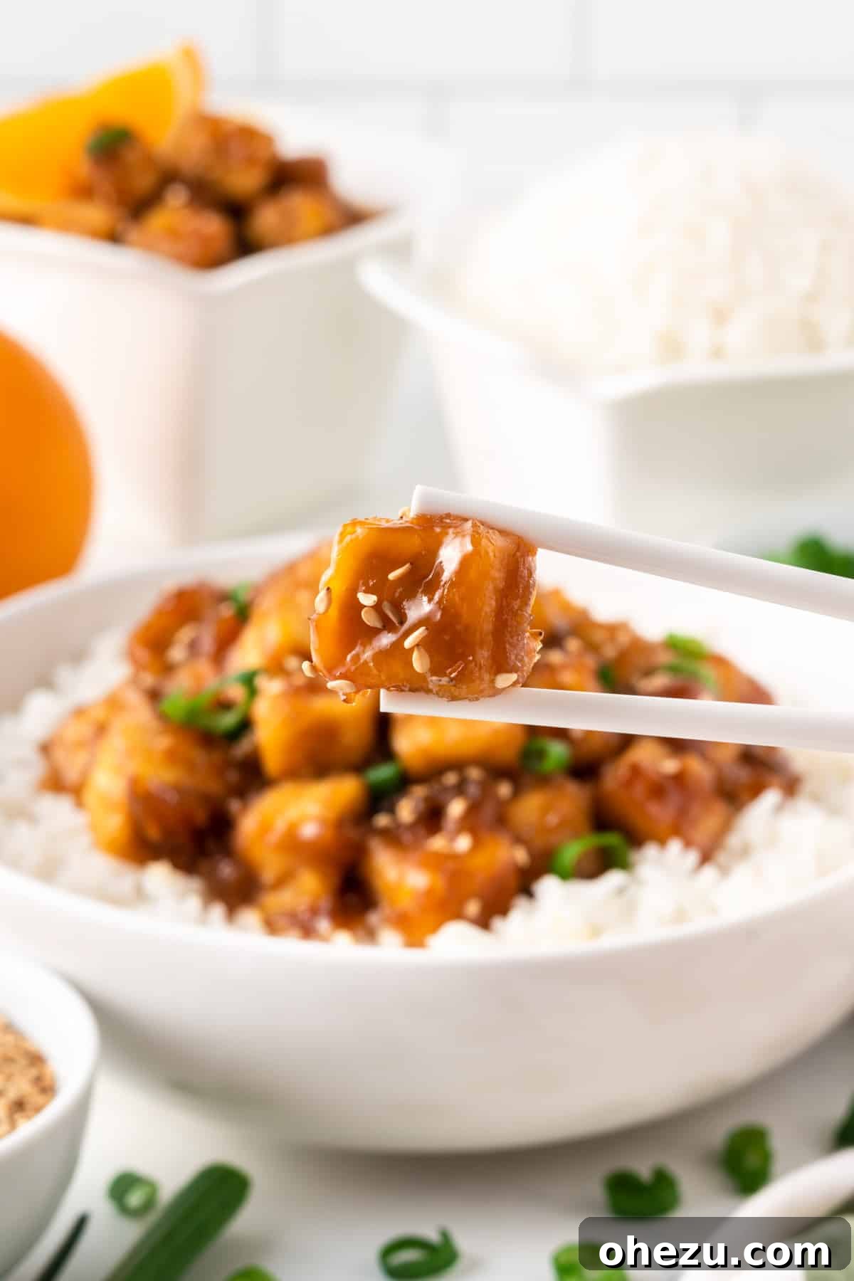 Chopsticks delicately holding a piece of perfectly glazed orange tofu, showcasing its golden crispiness.