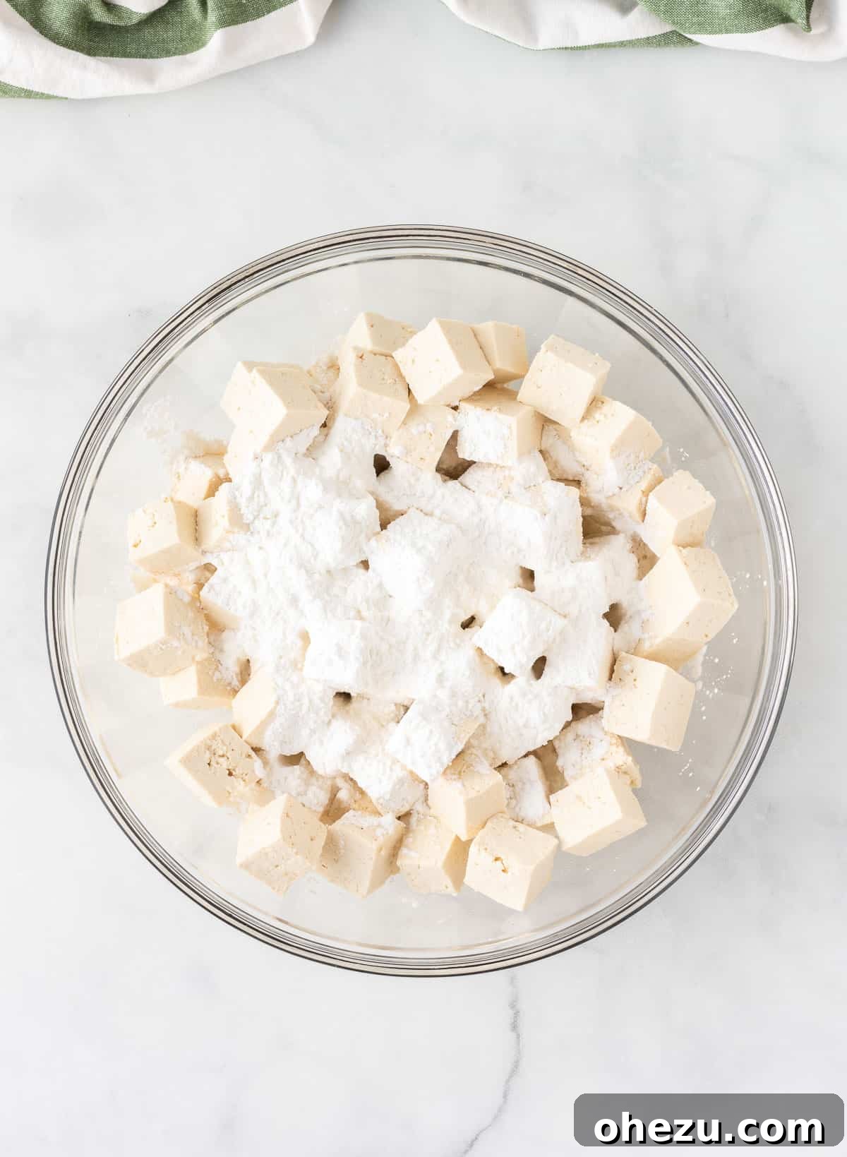 A bowl containing cubed tofu, generously dusted with white cornstarch, ready for coating.