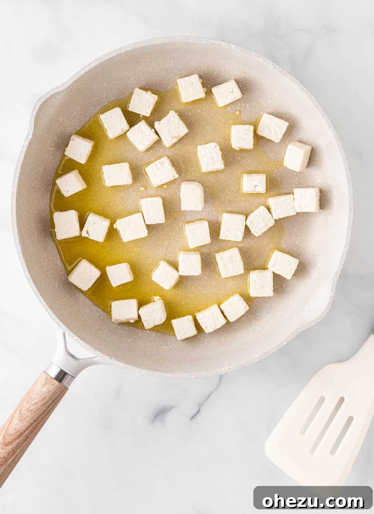 Crispy cornstarch-coated tofu cubes being added to a hot skillet containing olive oil.