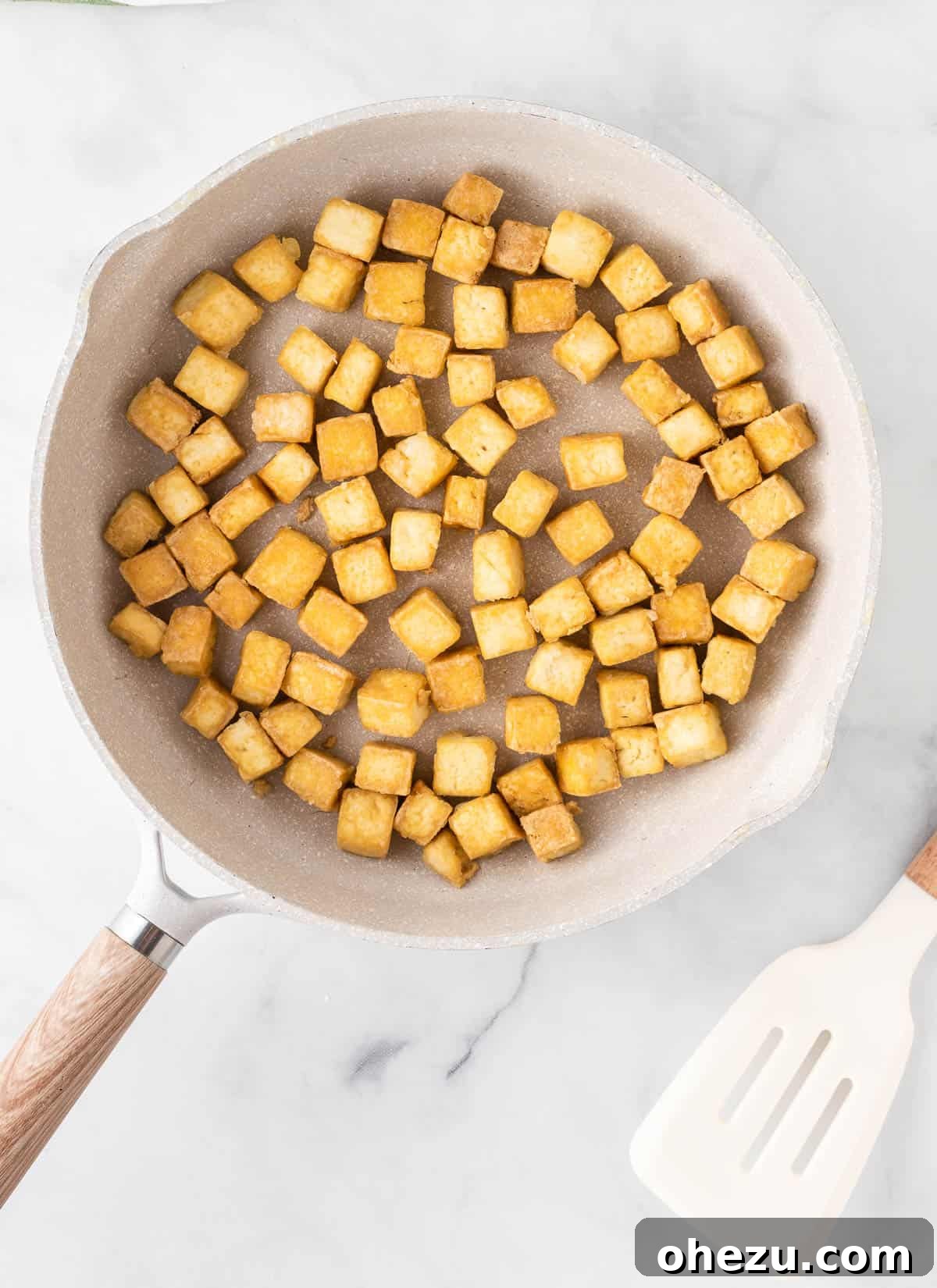 A skillet filled with perfectly golden-brown and crispy tofu cubes, ready to be coated in sauce.