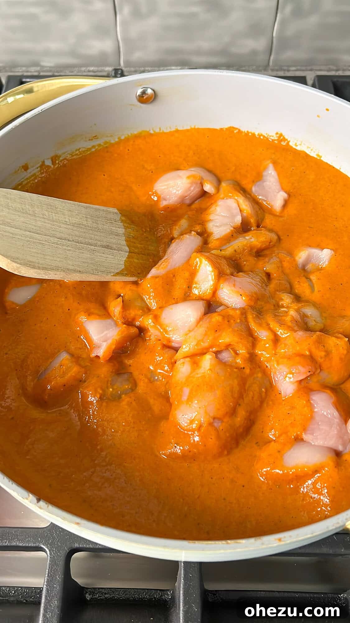 Effortless Butter Chicken 12 More chicken pieces being added and stirred into the rich, simmering butter chicken sauce.