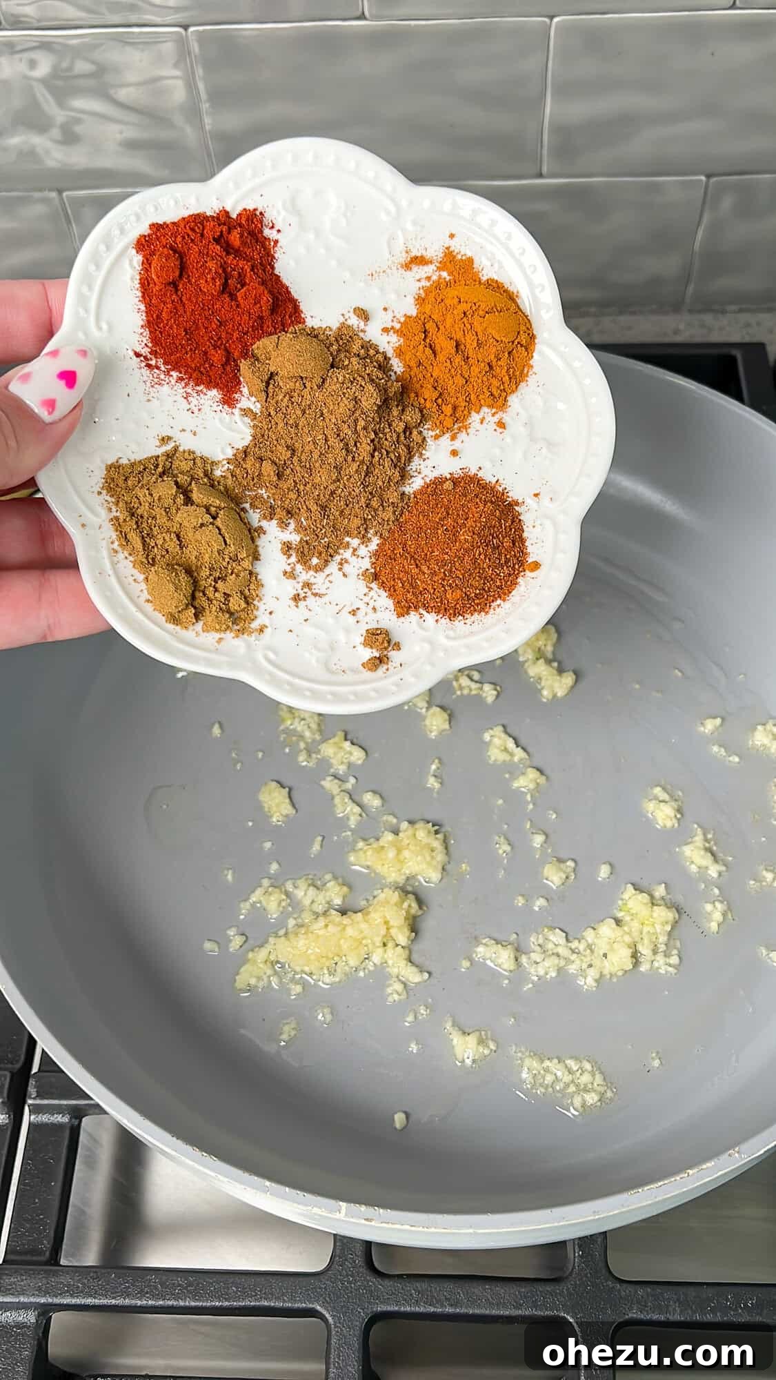 Effortless Butter Chicken 5 A hand sprinkling vibrant spices into a hot skillet with sautéed garlic and ginger.