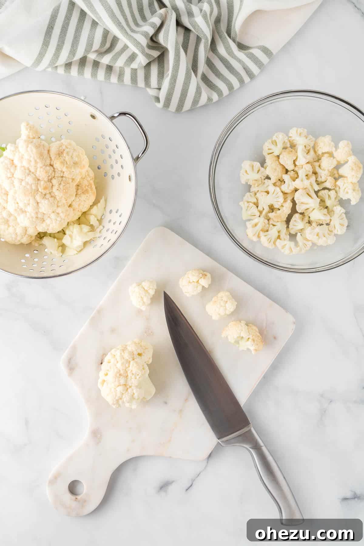 A person cutting a head of fresh cauliflower into florets on a wooden cutting board