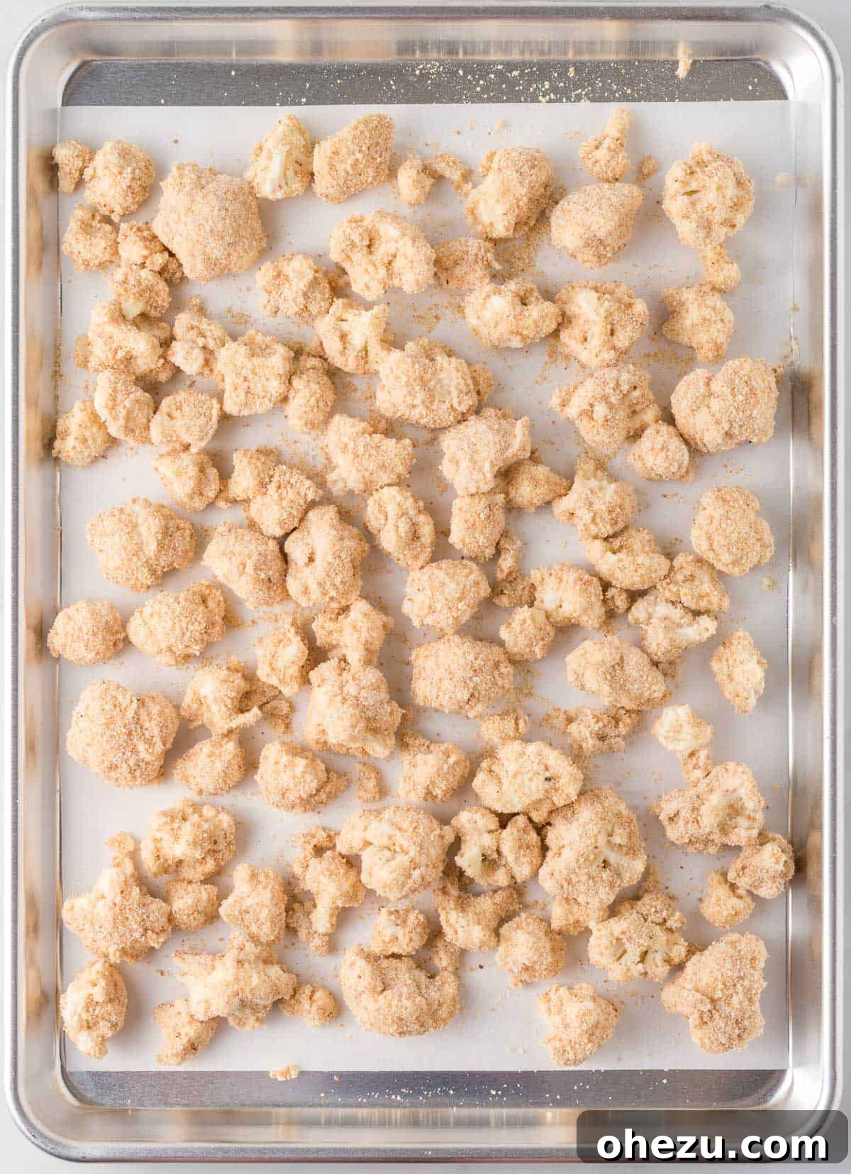 Breaded cauliflower florets arranged neatly on a parchment paper-lined baking sheet, ready for baking
