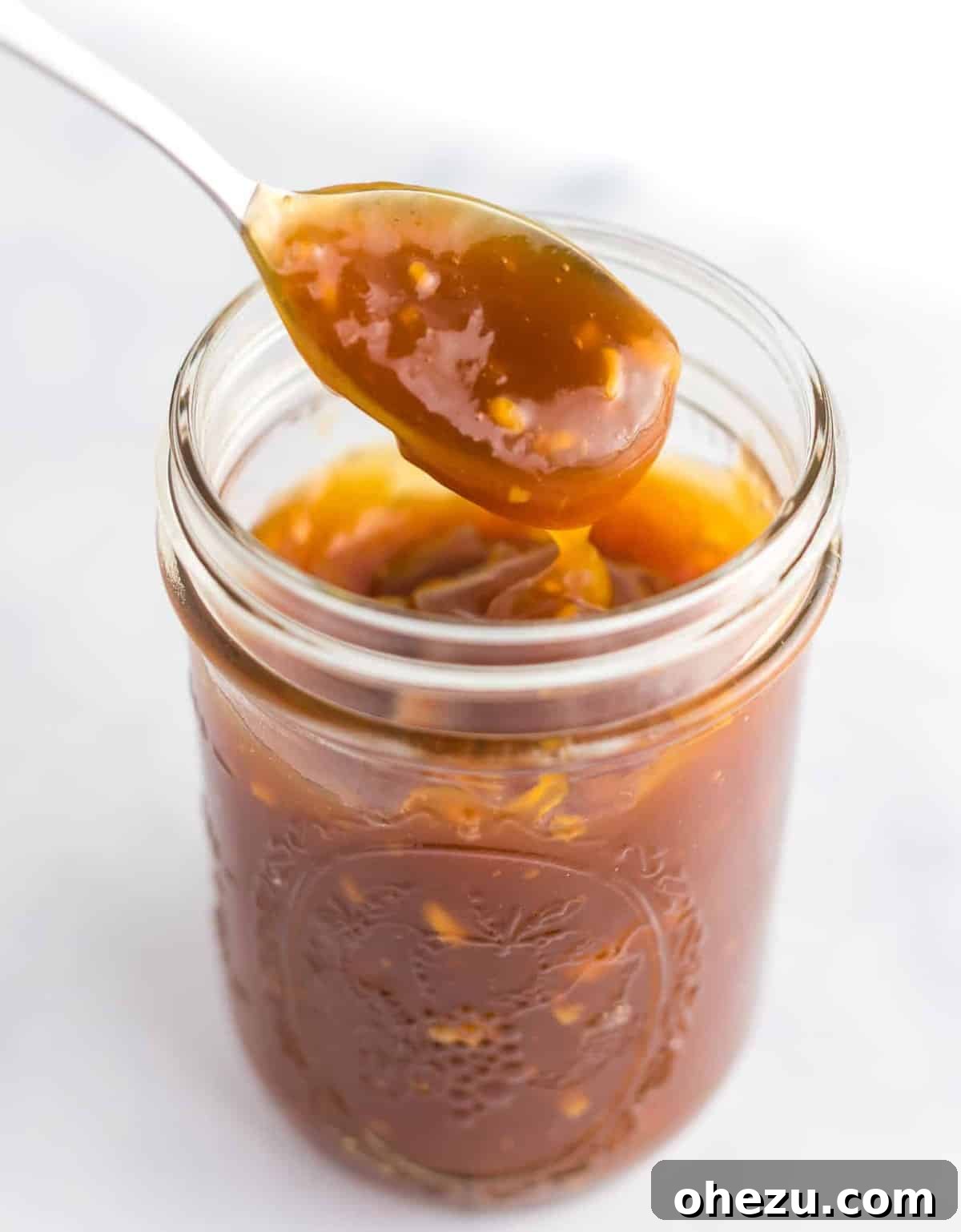 A spoon dipping into a rich, glossy homemade orange sauce, perfect for coating tofu or cauliflower