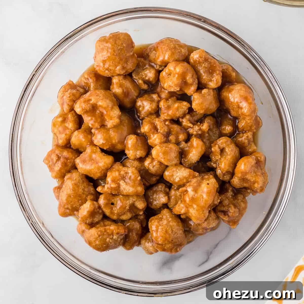Orange cauliflower florets coated in sauce, tossed in a large white bowl