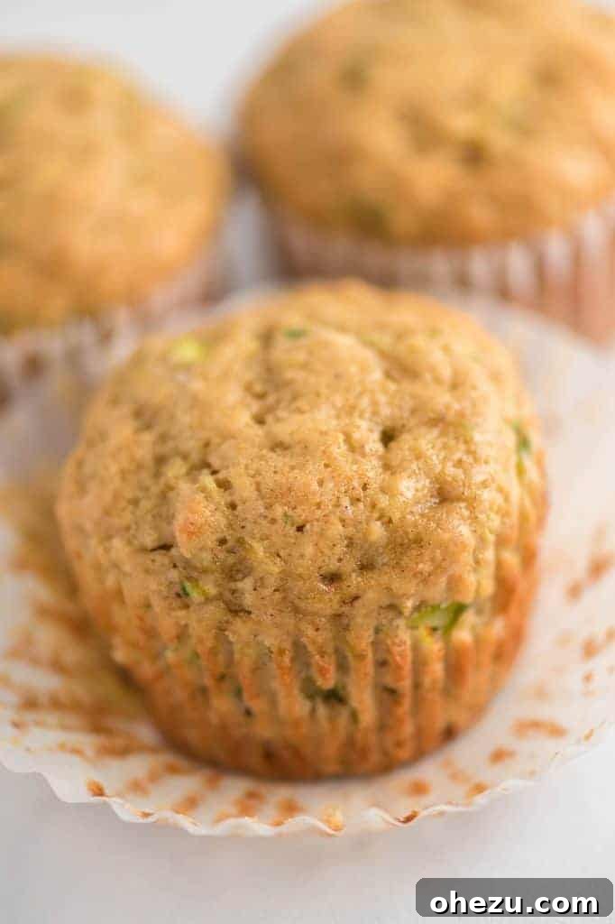 A single zucchini muffin, still perfectly nestled in its parchment paper liner, showcasing its inviting golden-brown top and delightful texture.