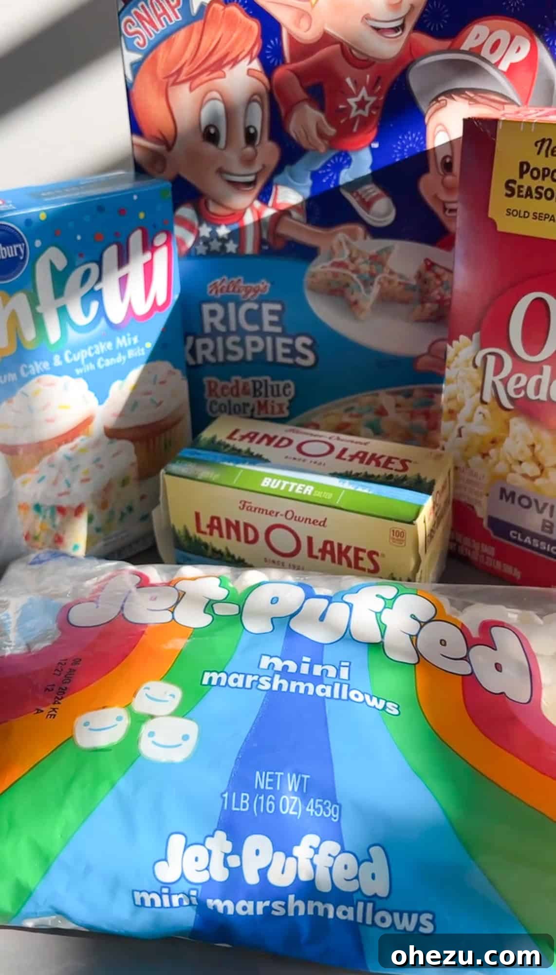 Birthday Cake Popcorn 3 A flat lay image displaying all the key ingredients needed to make funfetti cake batter popcorn, including butter, marshmallows, cake mix, and popcorn.