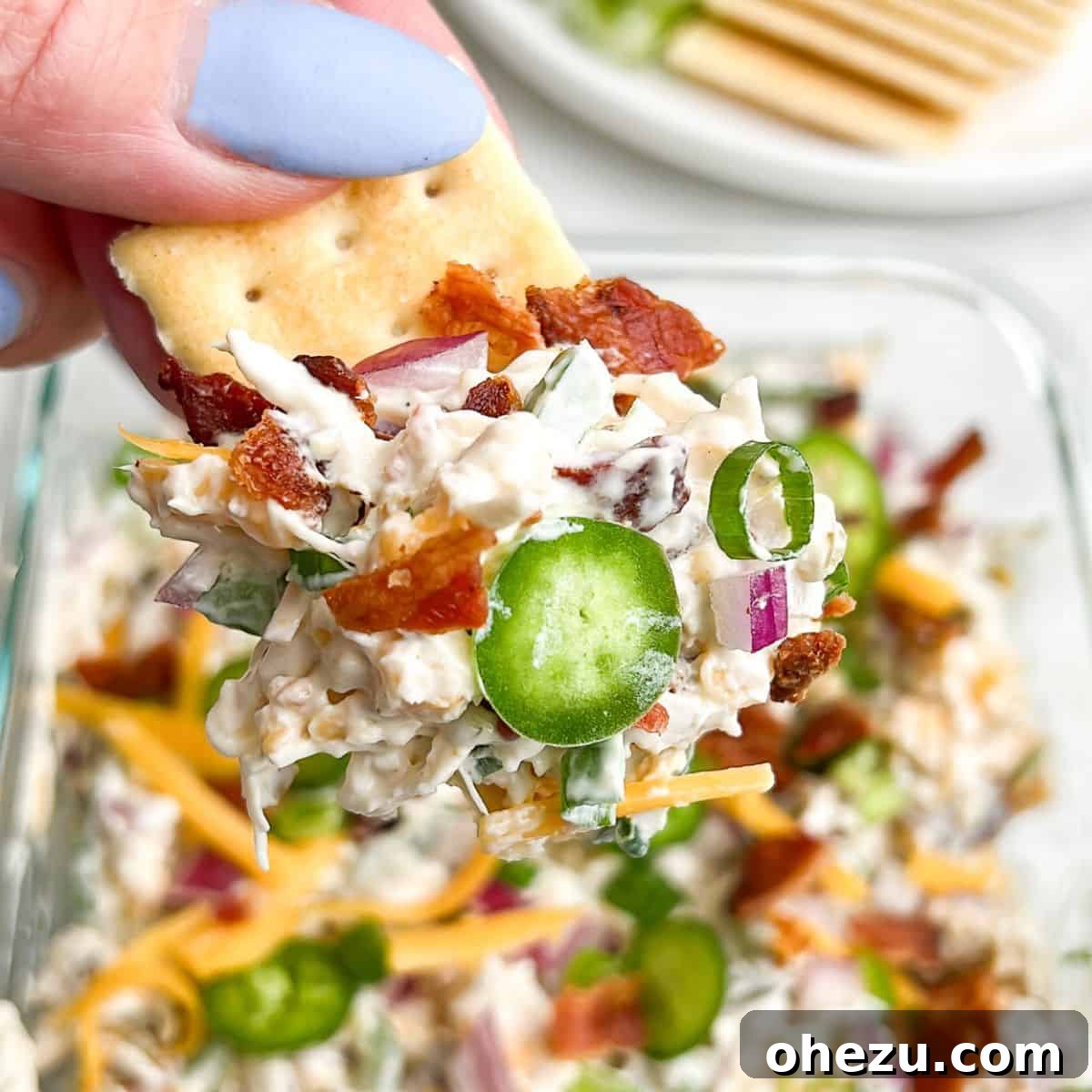 Jalapeno Popper Chicken Salad served on a cracker, held in hand, showcasing its creamy texture and vibrant ingredients.