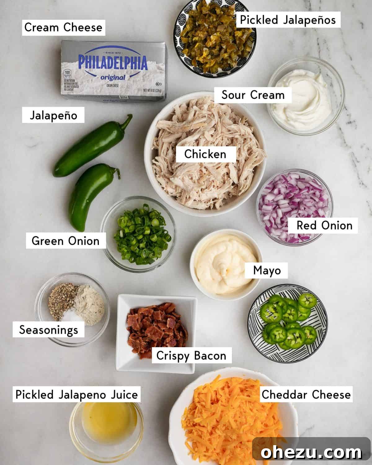 Various ingredients for chicken salad laid out on a table, including shredded chicken, jalapenos, bacon, and cheese.