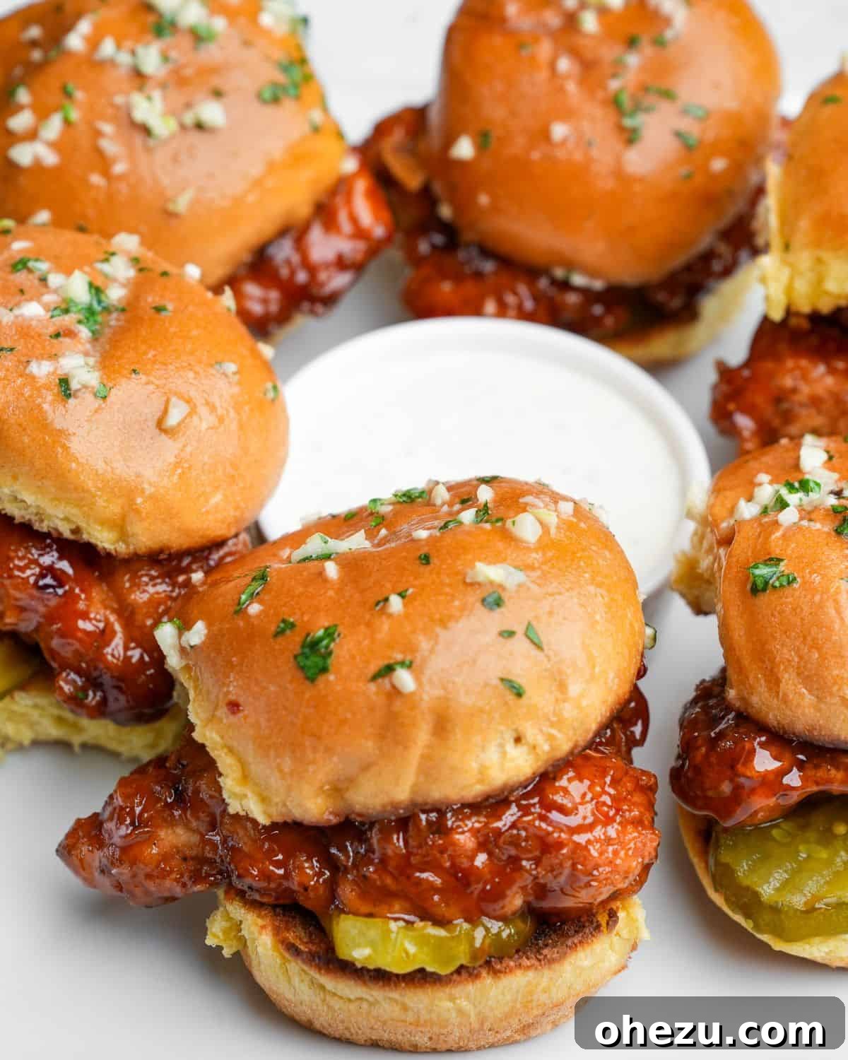 Delicious Hot Honey Chicken Sliders arranged artfully on a white plate, garnished with fresh parsley and served with a side of creamy ranch dipping sauce.