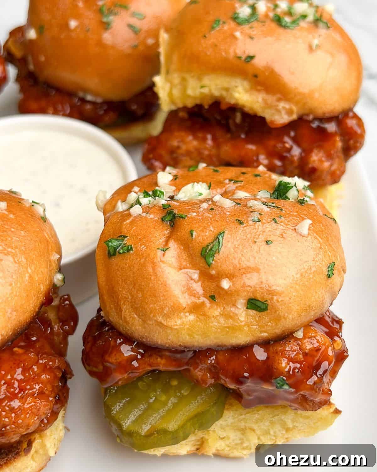 A beautifully presented platter of Hot Honey Chicken Sliders, garnished with fresh herbs, alongside a dipping bowl of creamy ranch dressing.