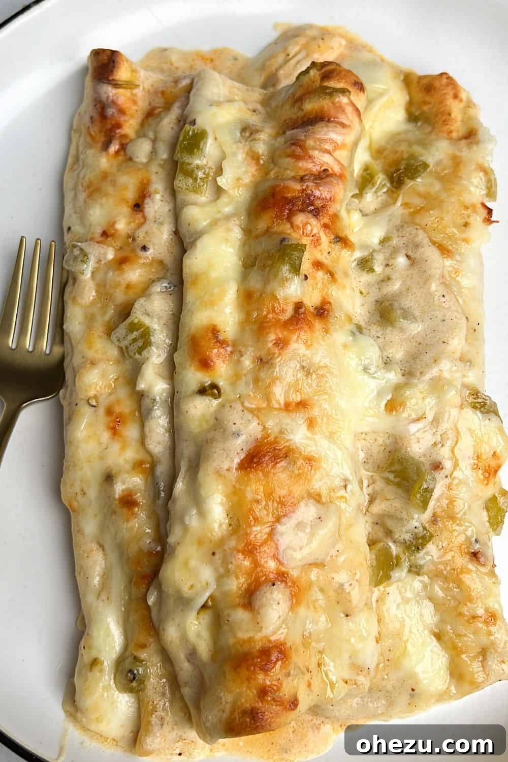 Southwestern Green Chile Chicken Enchiladas 2 Three perfectly baked white chicken enchiladas resting on a vibrant plate, generously covered in creamy green chile sauce and melted cheese, ready to be served.