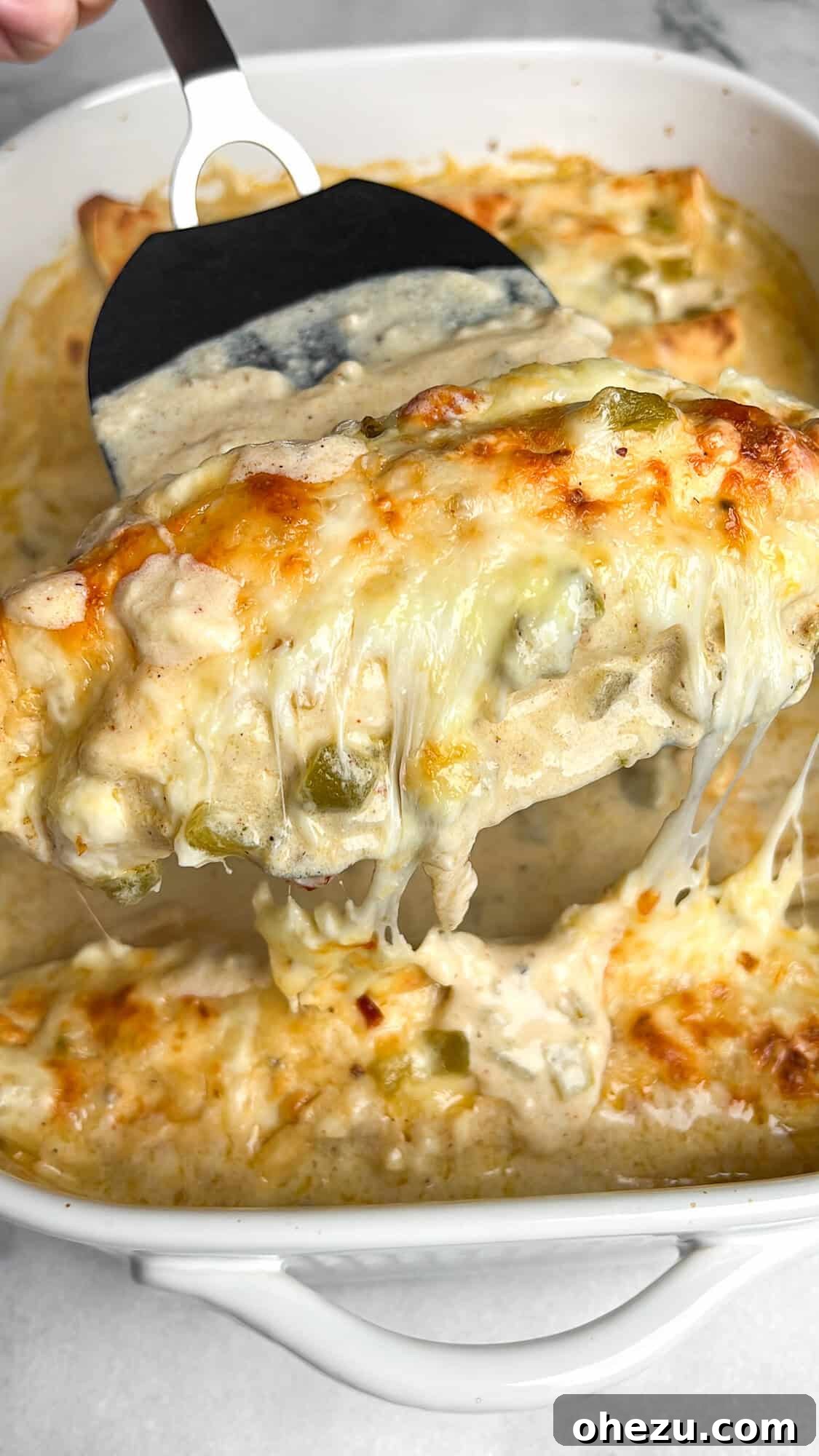 Southwestern Green Chile Chicken Enchiladas 11 A spatula scooping out a generous serving of baked green chile chicken enchiladas from a casserole dish, highlighting the gooey melted cheese and tender filling, ready for plating.