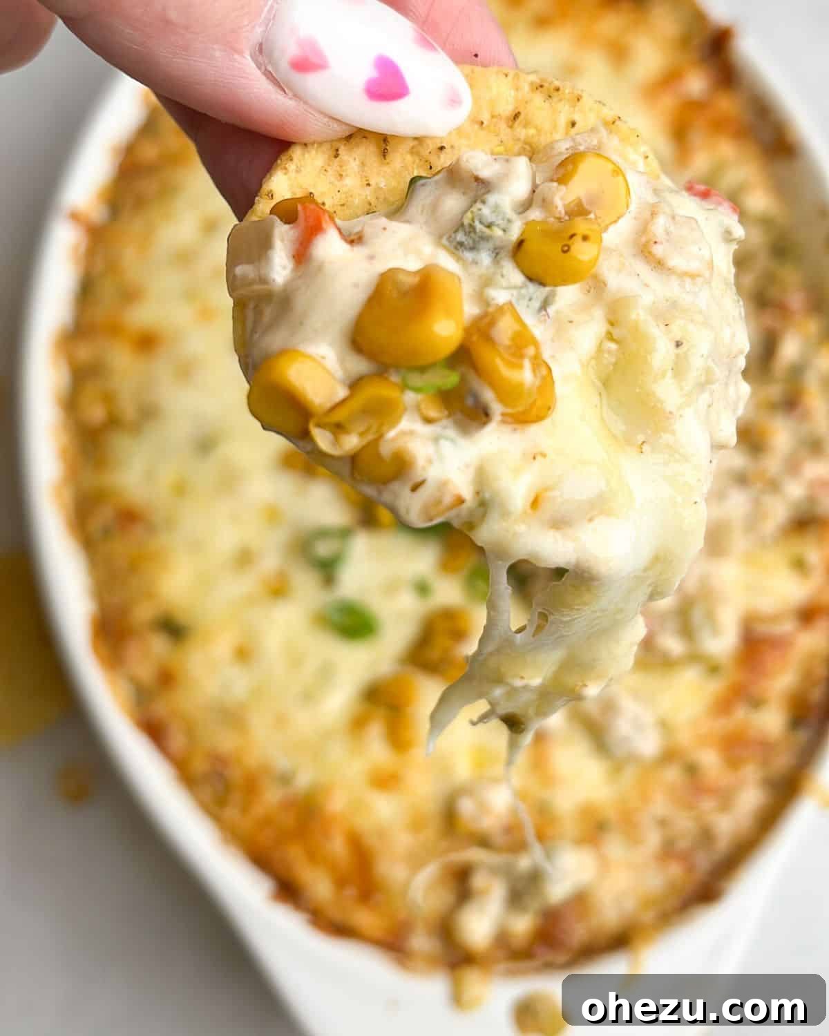 Close-up of hot corn dip scooped onto a crispy tortilla chip, showing its creamy texture and visible corn kernels and peppers.