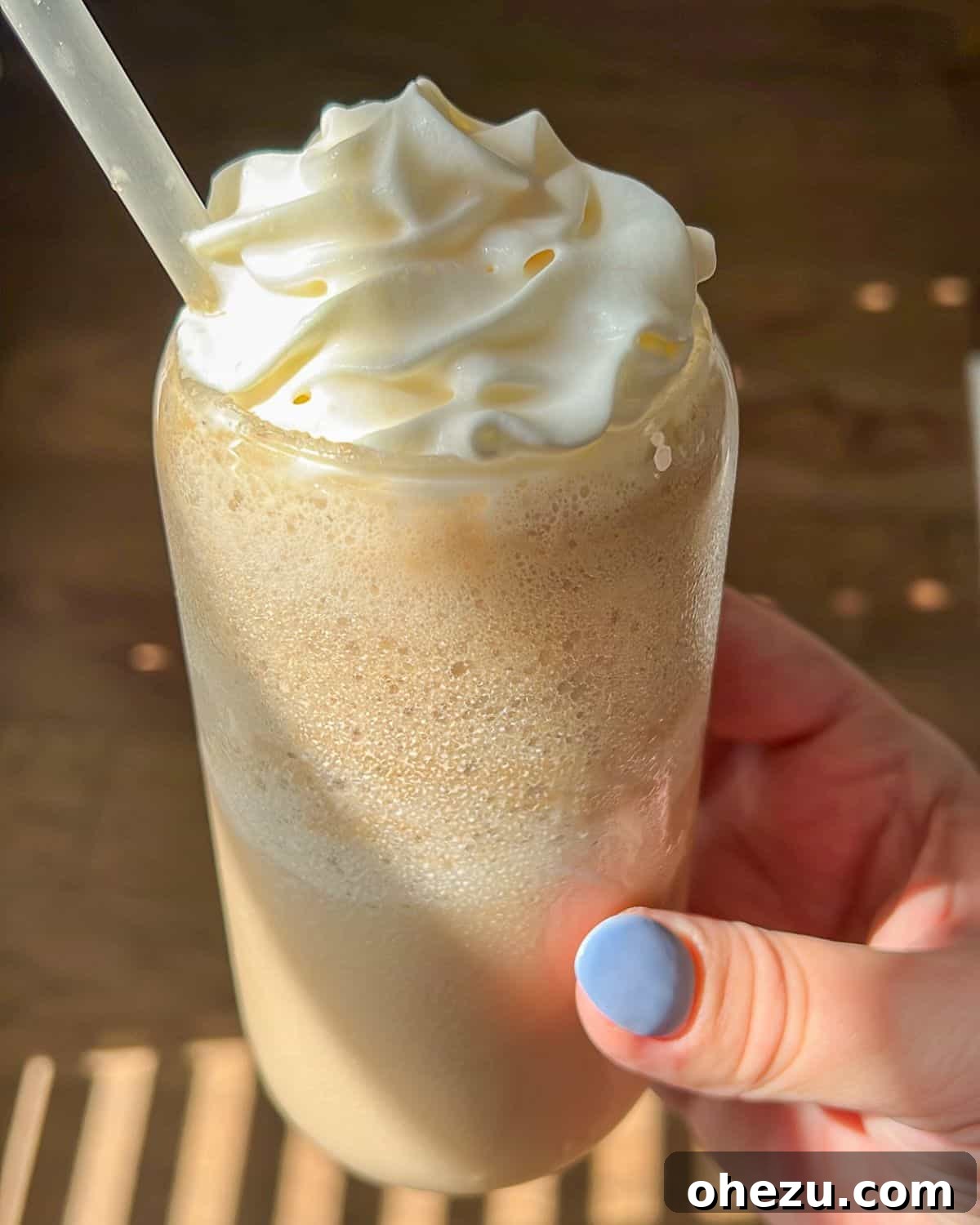 Hand holding a glass of whipped Dr. Pepper outdoors in natural sunlight, showcasing its creamy texture.