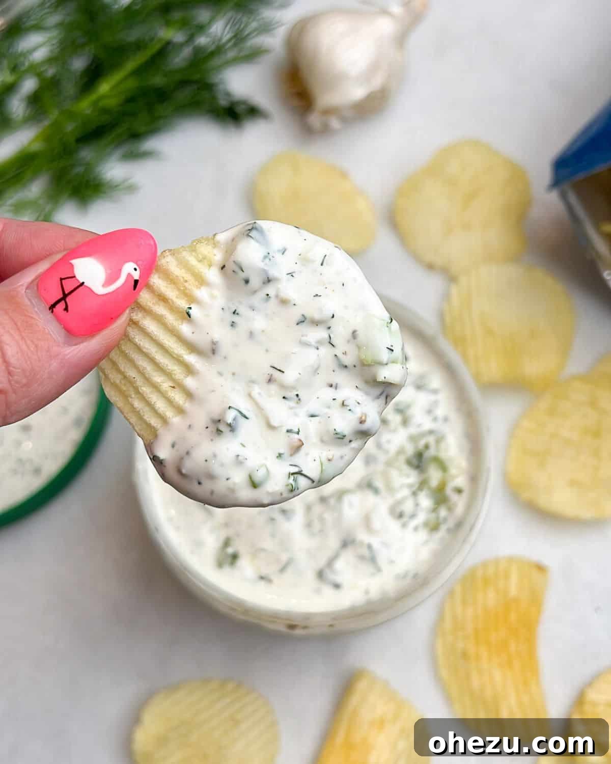 Dillicious Dip Sensation 6 A hand holding a potato chip generously dipped in creamy ranch pickle dip.