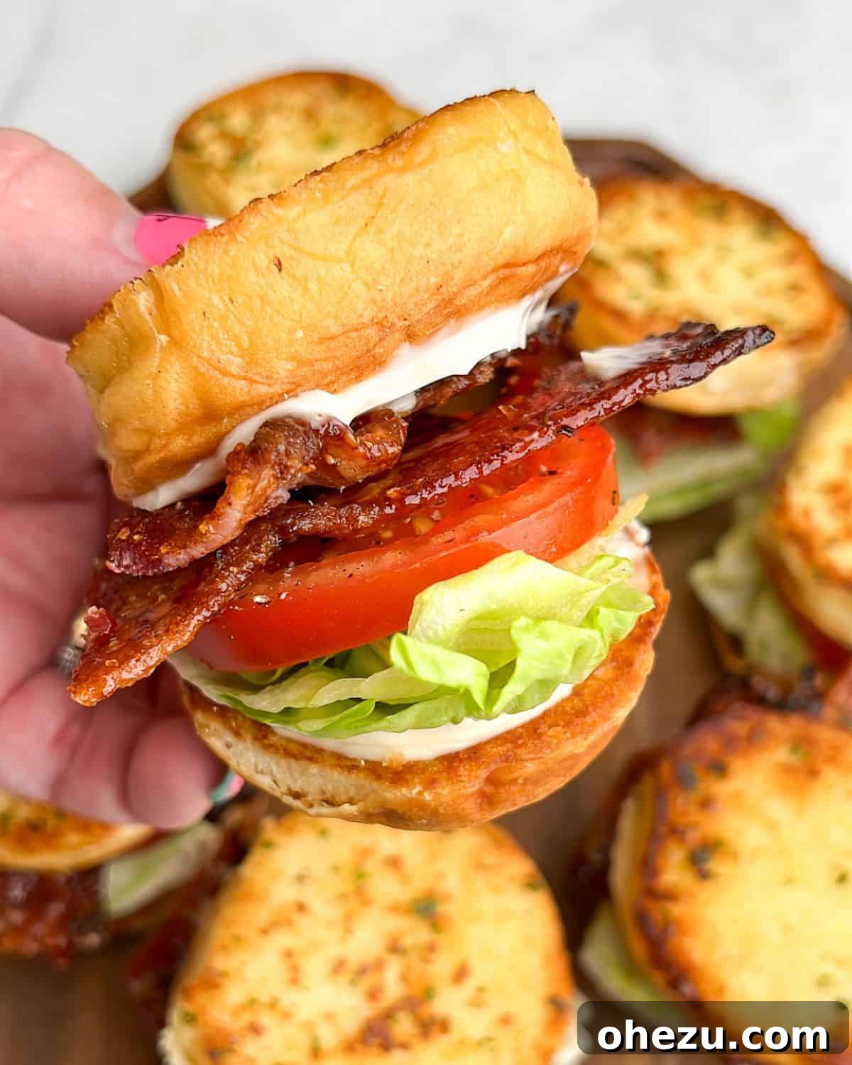 A tray of Candied Bacon BLT sliders on Hawaiian rolls, garnished with lettuce and tomato.