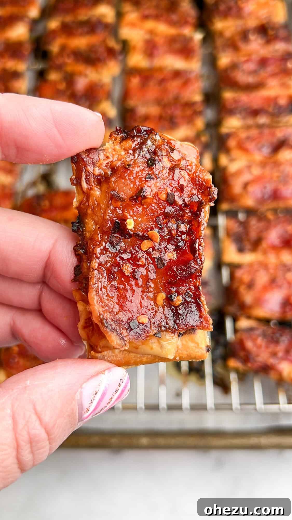 Close-up of crispy Parmesan Candied Bacon Crackers stacked on a white plate.