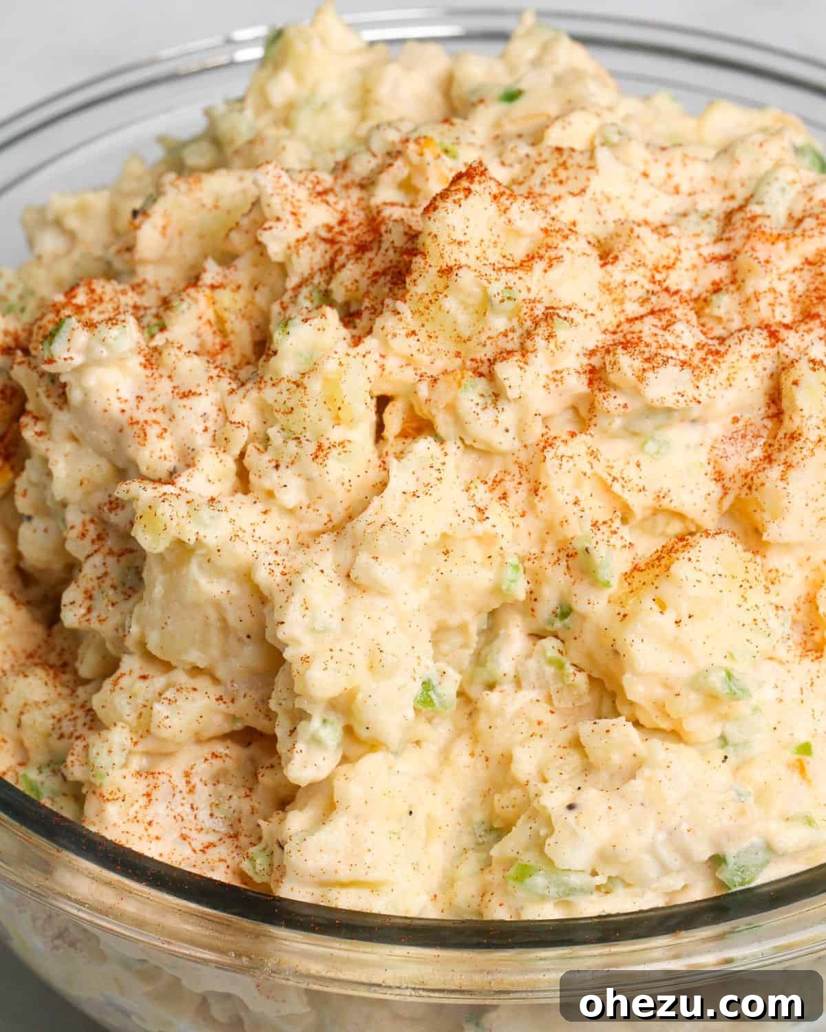 A serving bowl of creamy potato salad without eggs, garnished with fresh herbs.