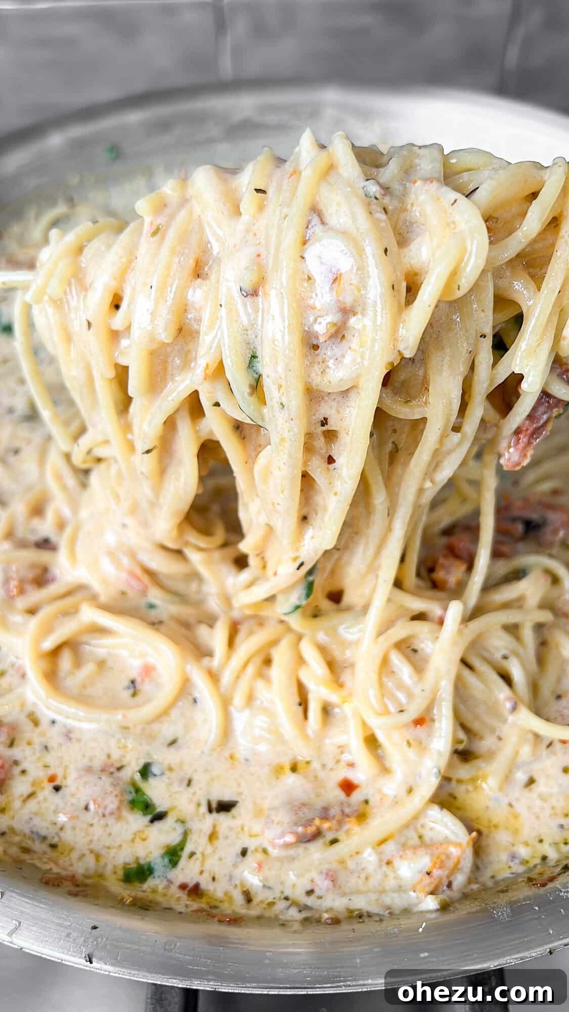 Tuscan Skillet Cream Pasta 8 Close-up view of thin pasta noodles cooking and absorbing a rich, creamy sauce in a pan.