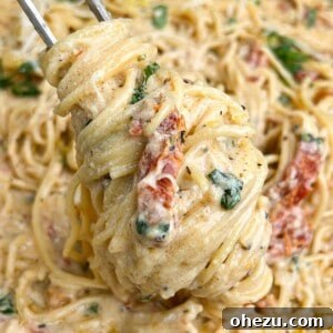 Pasta twirled around a fork, showcasing the creamy Tuscan sauce and fresh basil garnish.
