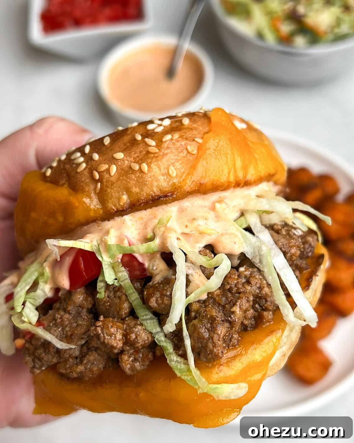 A close-up shot of a hand holding a perfectly assembled Tex-Mex Taco Burger, showcasing its delicious layers.