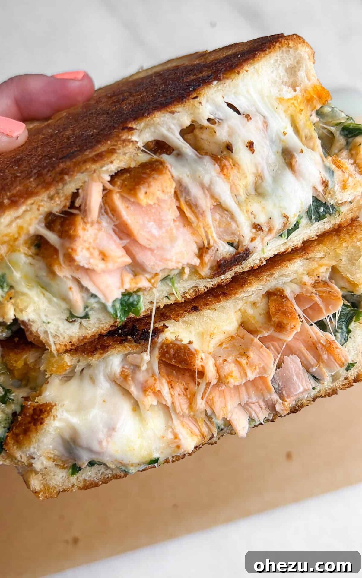 A salmon grilled cheese sandwich, cut in half to reveal the irresistible layers of filling.