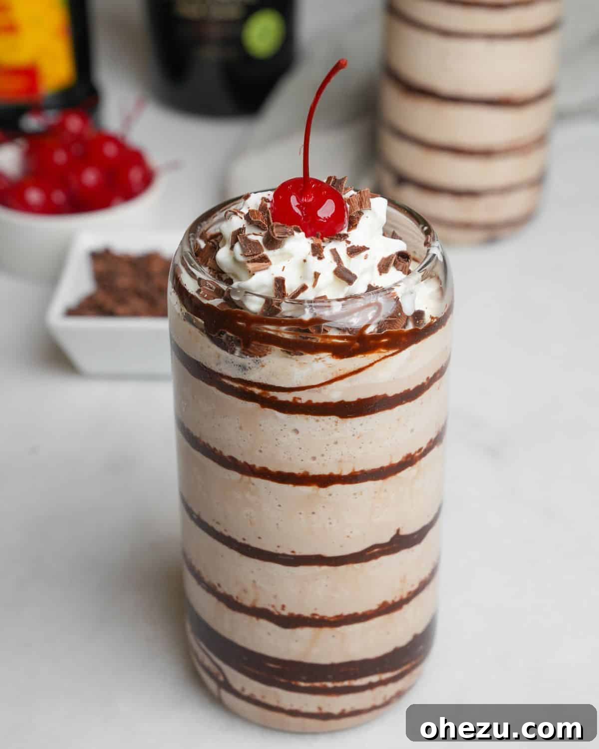 Two frozen mudslides on a table, garnished with chocolate shavings and cherries.