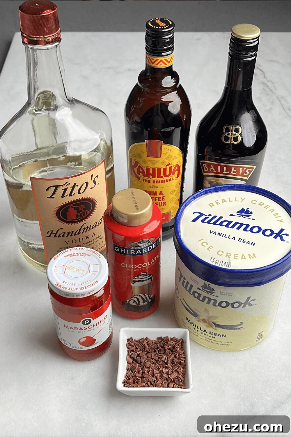 Ingredients for a mudslide boozy shake laid out on a kitchen counter, including bottles of Kahlua, Baileys, vodka, chocolate syrup, and a container of vanilla ice cream.