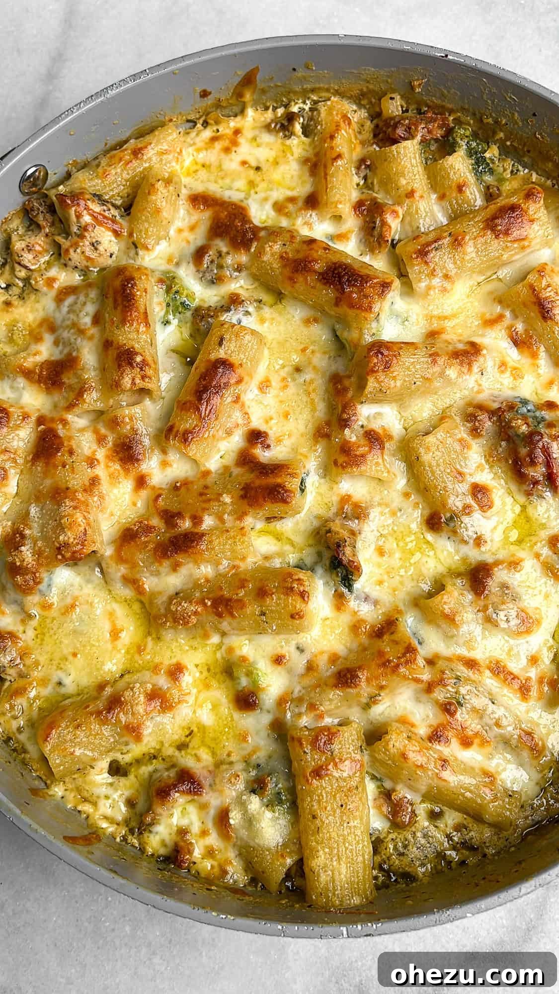 Overhead image of creamy pesto chicken pasta bake with golden-brown cheese and fresh basil garnish.