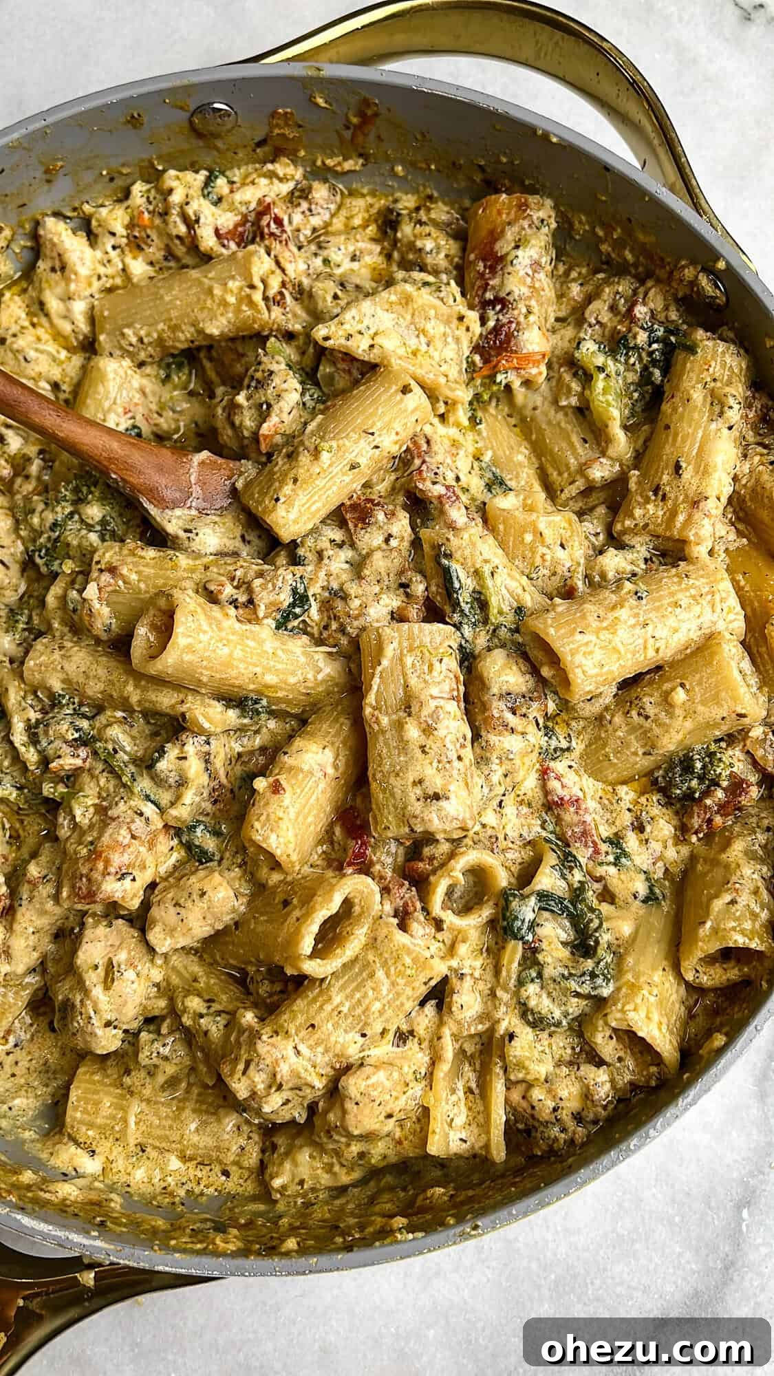 Overhead image of a large skillet filled with creamy pesto chicken pasta bake, garnished with fresh herbs, ready to be served.