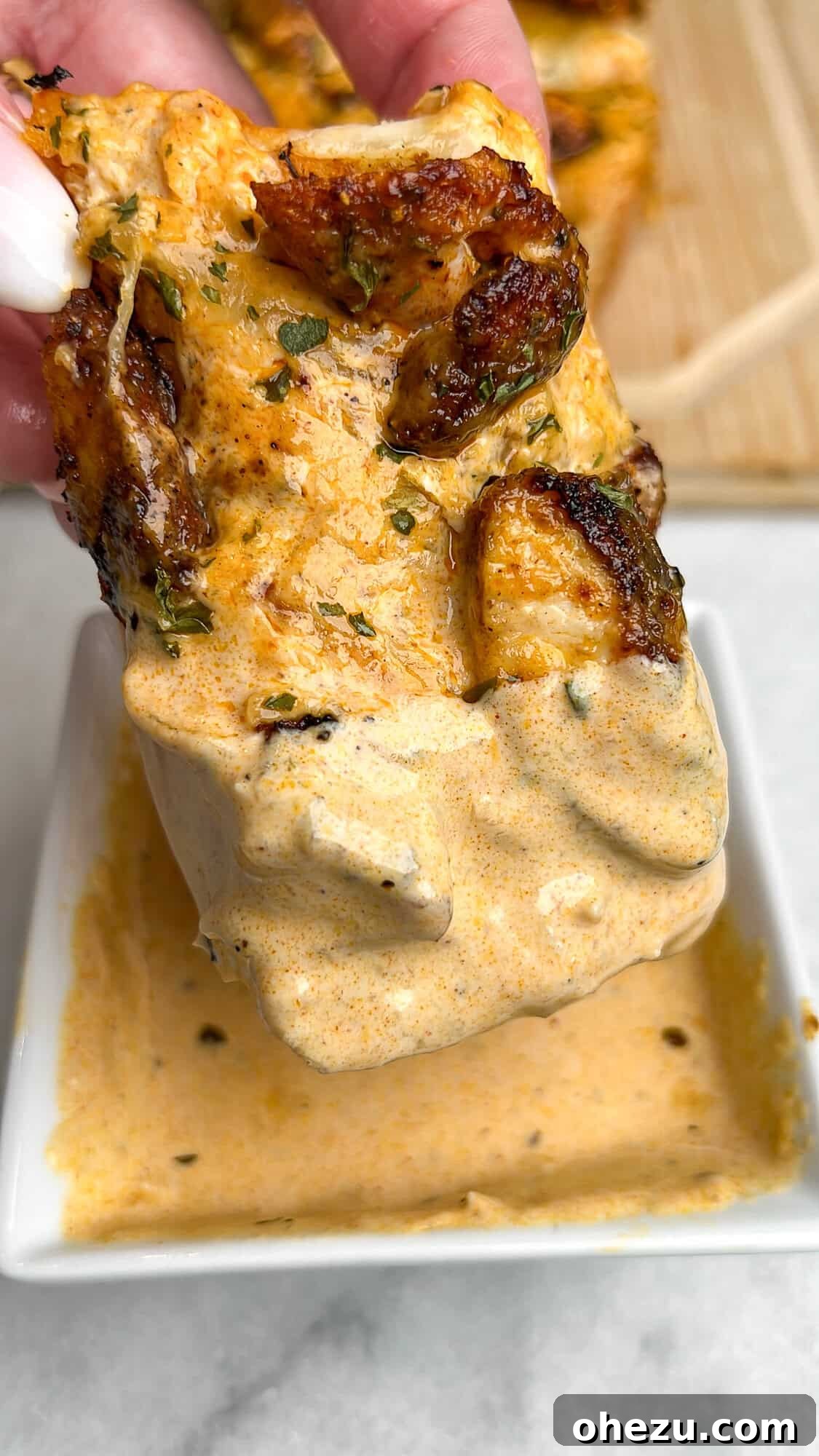 Dipping a piece of Chicken Alfredo Garlic Bread into a small bowl of Alfredo sauce.